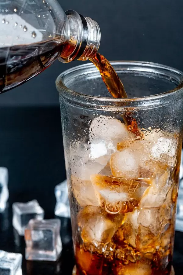 Pepsi is poured from a bottle into a glass with ice