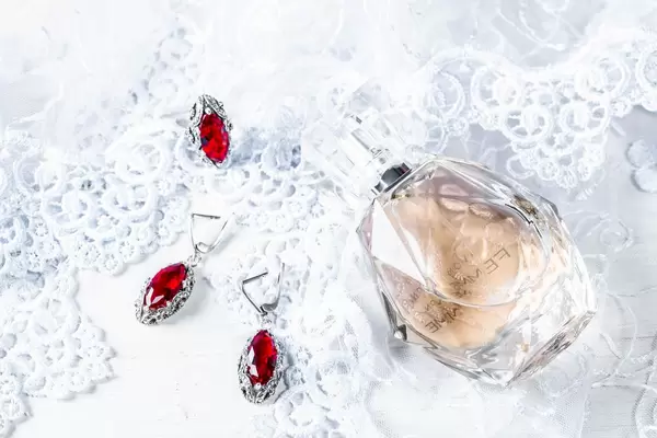 Perfume, earrings and ring with rubies on lace fabric