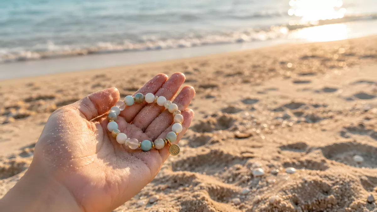 Perlenarmband mit Goldanhänger in Hand am Strand