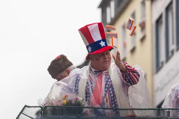 Persiflagewagen beim Kölner Karneval 2020: ein Mann im Stars and Stripes Anzug und Zylinder wirft Kamellen (Süßigkeiten) ins Publikum