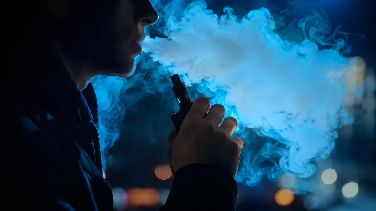 Person bläst Dampfwolke aus E-Zigarette bei Nacht