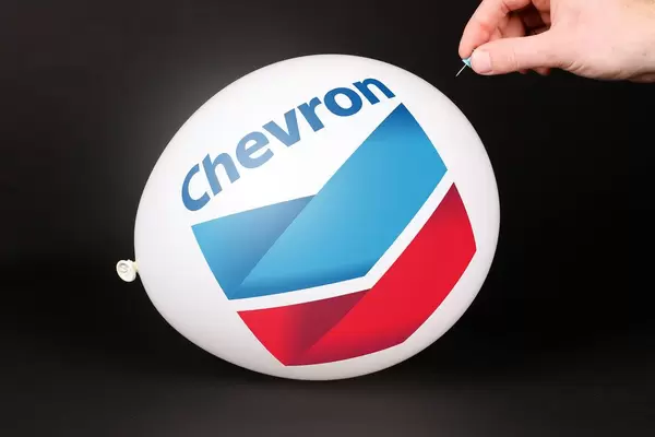 Person bringt einen Luftballoon mit Chevron Logo mit einer Stecknadel zum platzen mit schwarzem Hintergrund