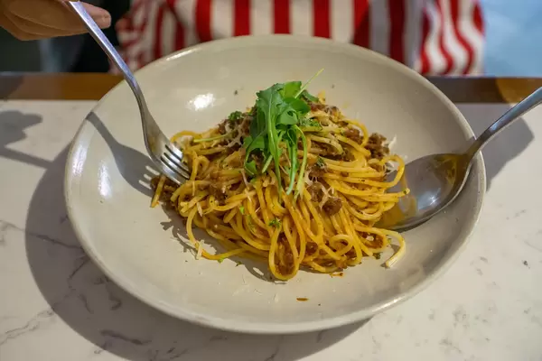Person eating Spaghetti Bolognese topped with Grated Cheese and Arugula with Fork and Spoon in a Restaurant