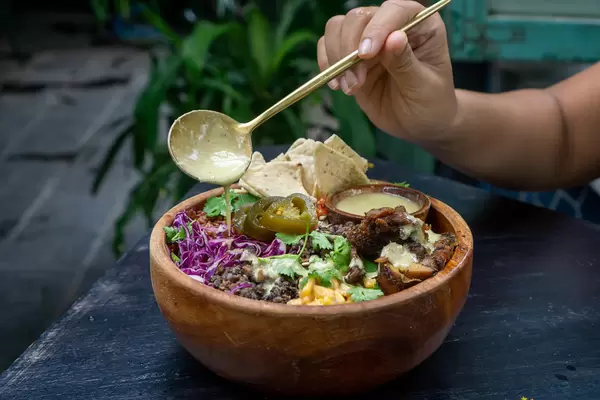 Person gibt Honig Senf Dressing auf eine gemischte Salat Bowl mit Bohnen, Jalapenos, gegrilltem Hähnchen, Mais, Tortilla Chips and Rotkohl mit einem Löffel in einem Restaurant