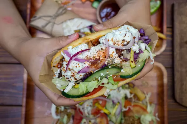 Person hält einen Döner Kebab mit Hähnchenfleisch, frischem Gemüse, Zwiebeln und Tzatziki Soße in beiden Händen von oben fotografiert