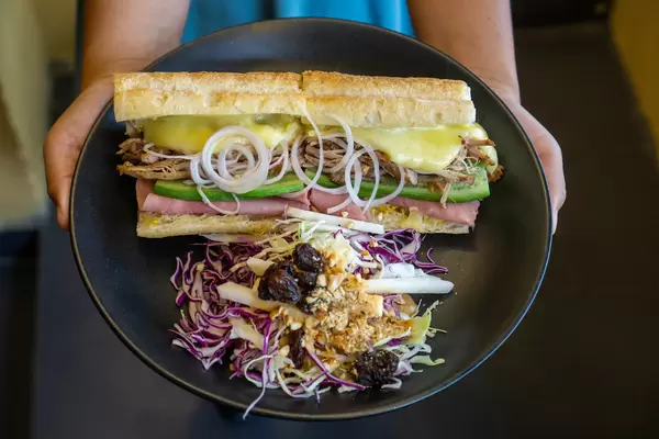 Person hält einen Teller in der Hand mit Pulled Pork Sandwich mit Schinken, Schweizer Käse und Coleslaw Salat mit Rosinen und Erdnüssen
