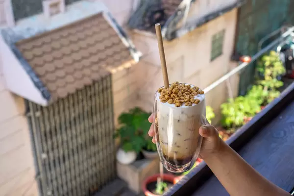 Person holding a Double Wall Latte Glass with Iced Vanilla Latte topped with Puffed Rice Cereals on a Balcony of a Cafe