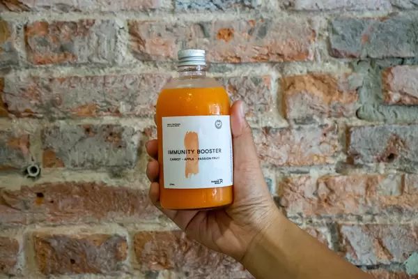 Person holding a Small Glass Bottle of Freshly Pressed Juice with Carrot, Apple and Passion Fruit as Immunity Booster in front of rustic Background