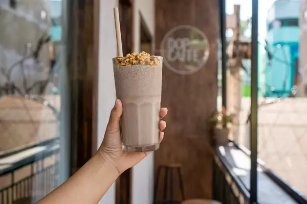 Person holding Cocktail Glass with Cookies and Cream Milkshake, Puffed Rice and Paper Straw on a Balcony of a Cafe
