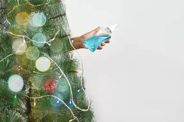 Person holding hand sanitizer from behind of Xmas tree