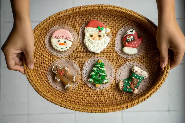 Person holding Oval Rattan Tray with Christmas Gingerbread Cookies in different Forms with both Hands