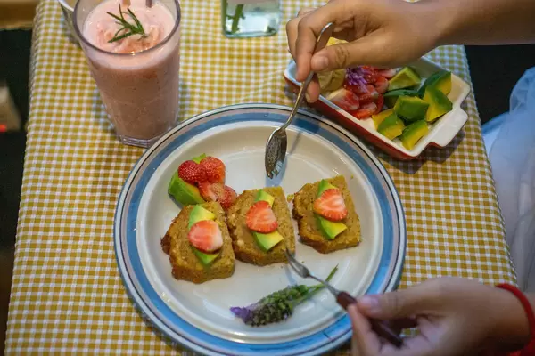 Person is eating Carrot Cake with Strawberries and Avocado with Spoon and Fork Top View