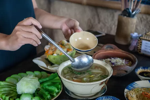 Person is using a Ladle to get Sour Soup with many different Dishes on the Table in a Restaurant in Saigon, Vietnam
