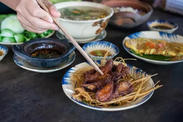 Person is using Wooden Chopsticks to pick Food from different Plates in a Vietnamese Restaurant