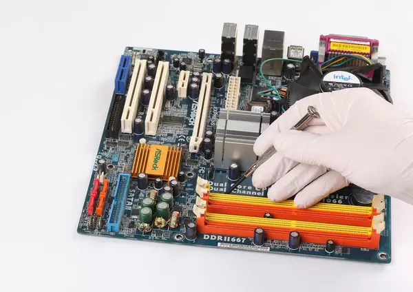 Person mit Gummihandschuhen hält einen Schraubenzieher über einer Hauptplatine eines Computers auf weißem Hintergrund