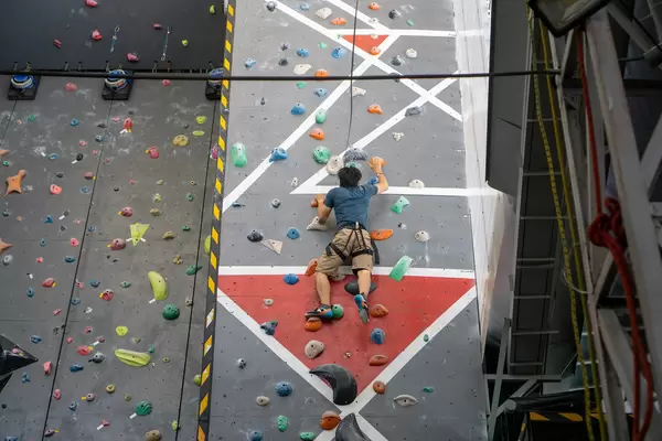 Person mit Sicherheitsgurt und Kletterschuhen klettert auf einer Wand mit Griffen in einer Indoor-Kletterhalle