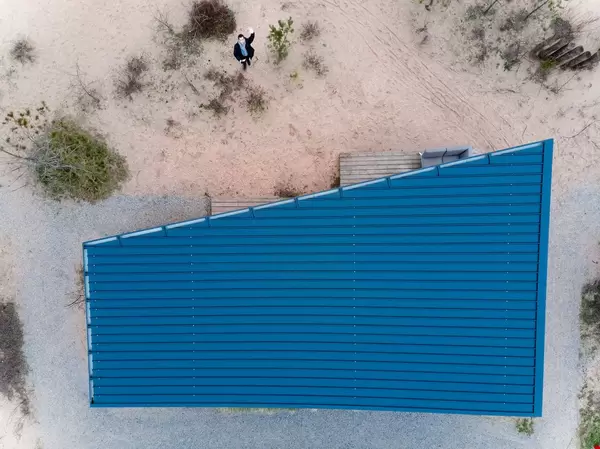 Person neben Haus mit asymmetrischem blauem Dach winkt Drohne zu