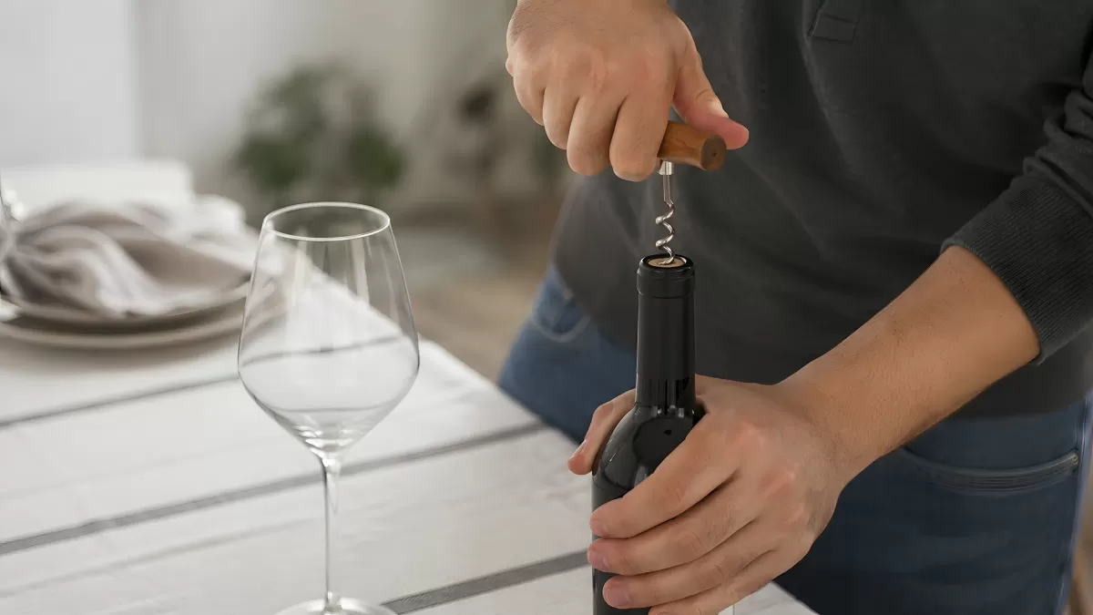Person öffnet Rotweinflasche mit Korkenzieher am Tisch