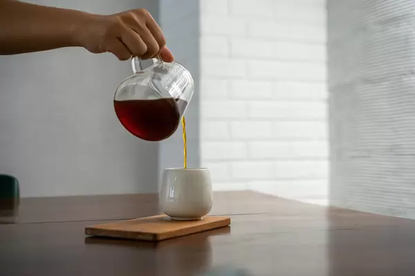 Person pouring Hot Coffee from a Glass Jug into a White Ceramic Cup in a modern Cafe
