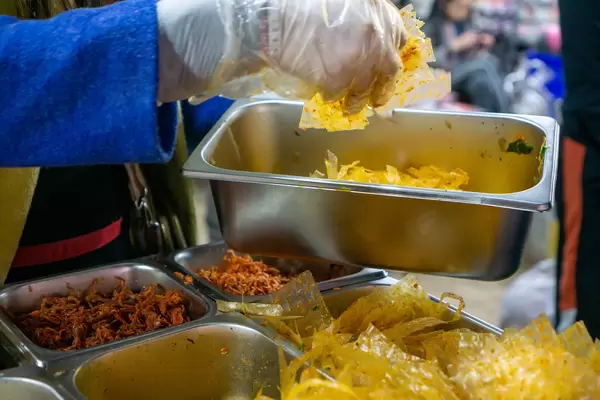 Person preparing Vietnamese Mixed Rice Paper Snack Banh Trang Tron with different Ingredients at a Night Market in Dalat, Vietnam