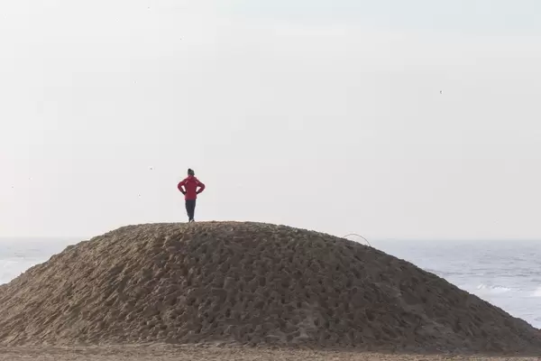 Person steht auf Sandhügel und blickt auf das Meer und die Wellen
