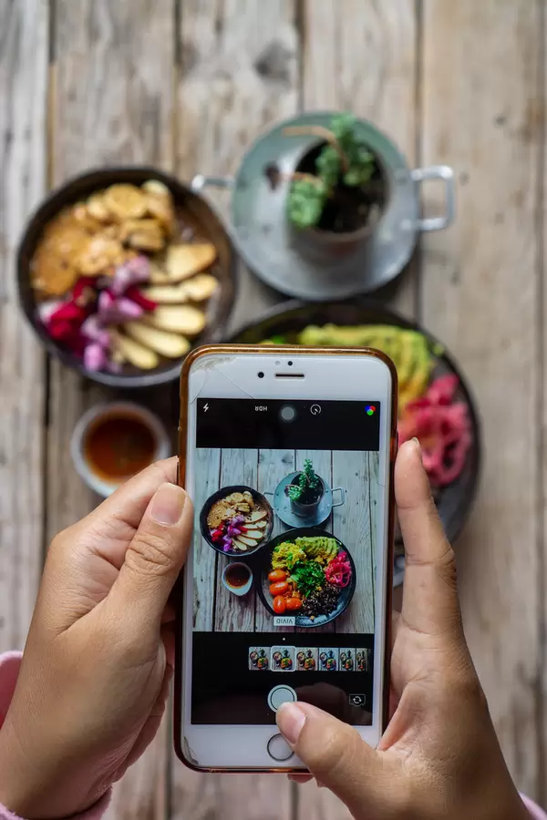 Person taking a Food Photo with an iPhone for Instagram of a Healthy Vegan Breakfast on a Wooden Table
