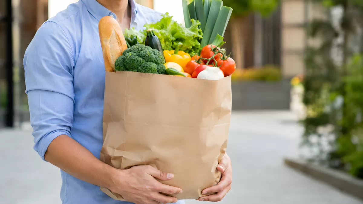 Person trägt Papiertüte mit frischem Gemüse und Brot