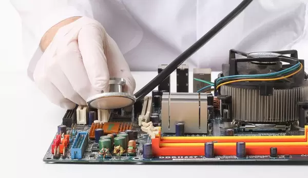 Person trägt Gummihandschuhe und hält ein Stethoskop über eine Hauptplatine eines Computers