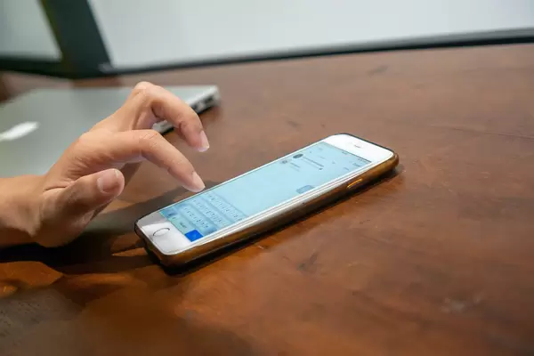 Person using the Keyboard of iPhone Smartphone to search on Instagram with Apple Macbook in the Background