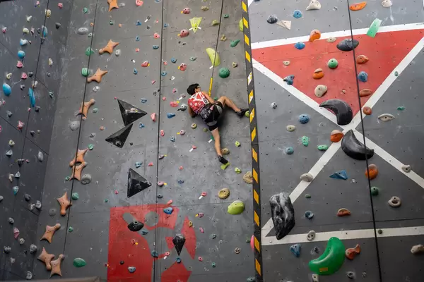Person with Safety Harness and Climbing Shoes is attached to a Rope and Climbing up a Wall in an Indoor Climbing Hall