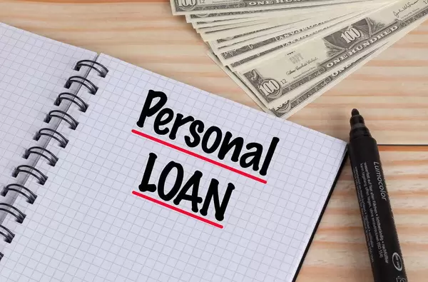 Personal Loan text in notebook and Dollar banknotes on wooden table