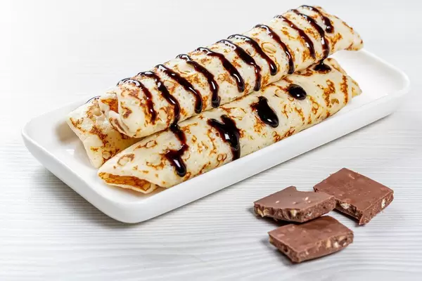 Pfannkuchen mit Schokoladensoße und Schokowürfeln auf einem Holztisch