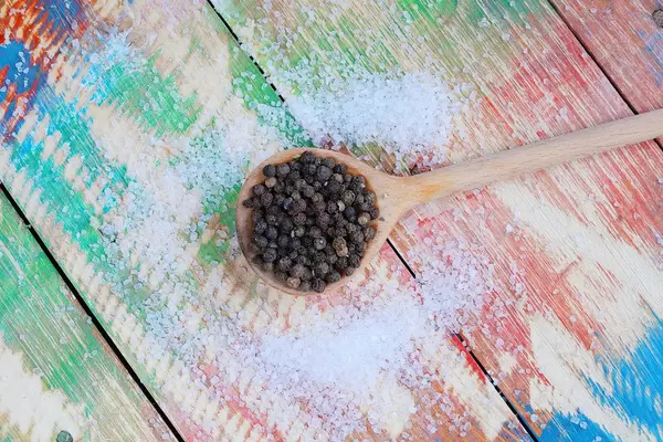 Pfefferkörner in einem Holzlöffel mit Salz auf einem bunten Holztisch im Vintage-Stil