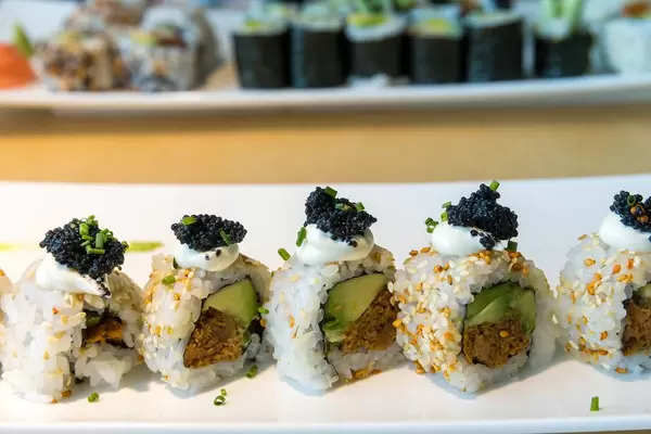 Pflanzliches Hauptgericht mit veganem Sushi, gefüllt mit Avocadoscheiben, Frühlingszwiebeln, würziger Sauce, Sesamkernen und veganem Kaviar