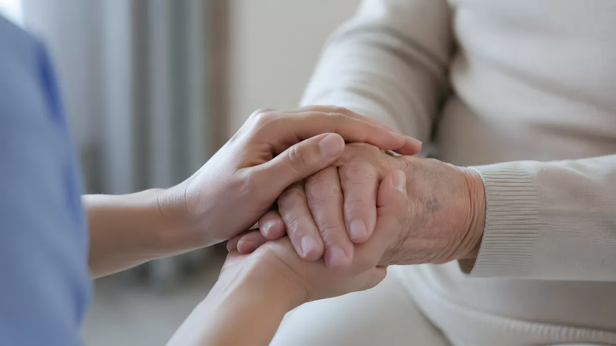 Pflegekraft hält fürsorglich die Hände einer älteren Person