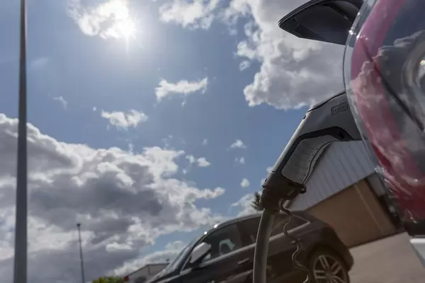 Phoenix Contact Type 2 plug is used to charge the Tesla Model 3 with sun energy at an Aldi-Süd parking lot, with clouds in front of the sun
