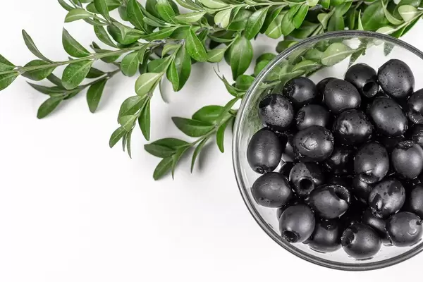 Pickle black olives in a glass bowl and branches withgreen leaves