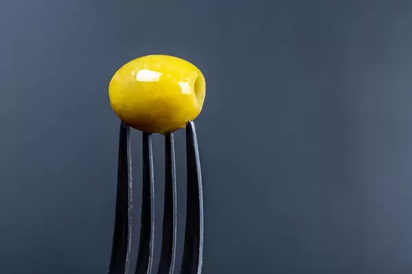 Pickled green olive on a fork on a dark background