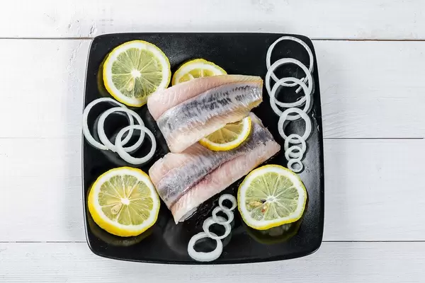 Pickled herring with lemon and onion on a black plate