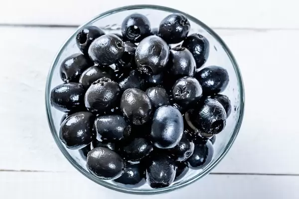 Pickled olives in glass bowl on white background, top view