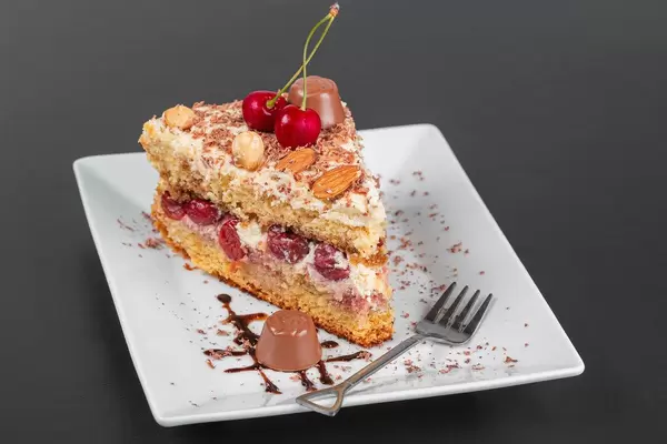 Piece of cake with cherries, chocolate and nuts on a plate with a fork