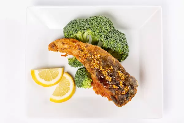 Piece of fried carp fish with broccoli and lemon, top view