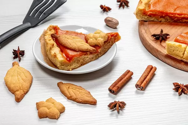 Piece of pumpkin pie with cinnamon, anise stars and cookies on a white table (Flip 2019)