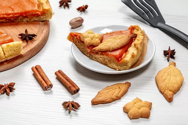 Piece of pumpkin pie with cinnamon, anise stars and cookies on a white table