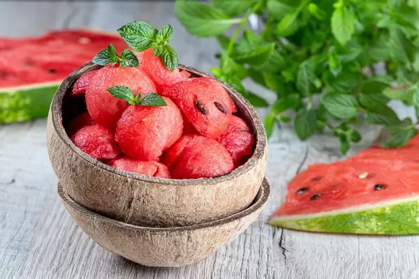 Pieces-balls of fresh red watermelon in a wooden bowl with mint leaves