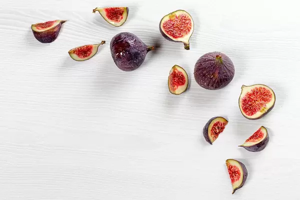 Pieces of fresh figs and whole fruit on a white wooden background with water drops (Flip 2019)