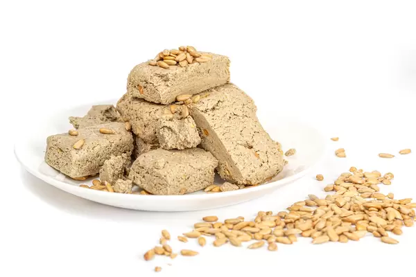 Pieces of halva with nuts in plate on white