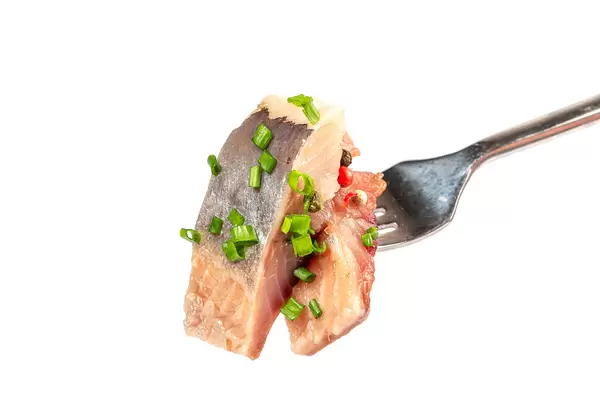 Pieces of salted herring on fork on white background