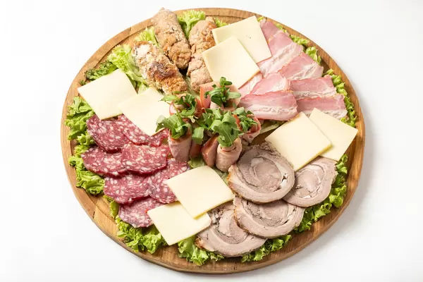 Pieces of smoked meat, sausages, cheeses and meat rolls with herbs on white