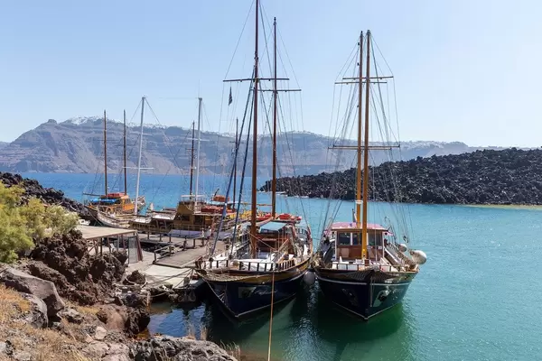 Pier in Santorini with four sailboats and the beautiful coast with cliffs in the background